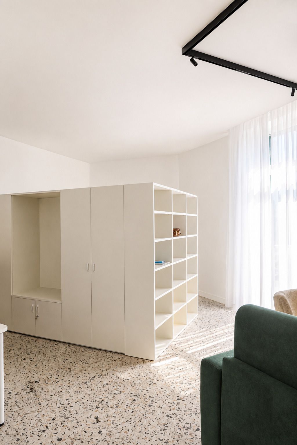 Una habitación con un armario blanco, estanterías, un sofá verde y un piso moteado.
