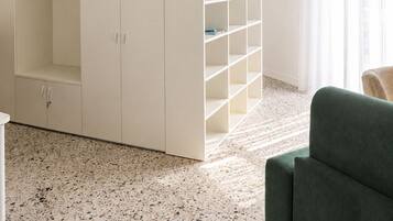 Una habitación con un armario blanco, estanterías, un sofá verde y un piso moteado.