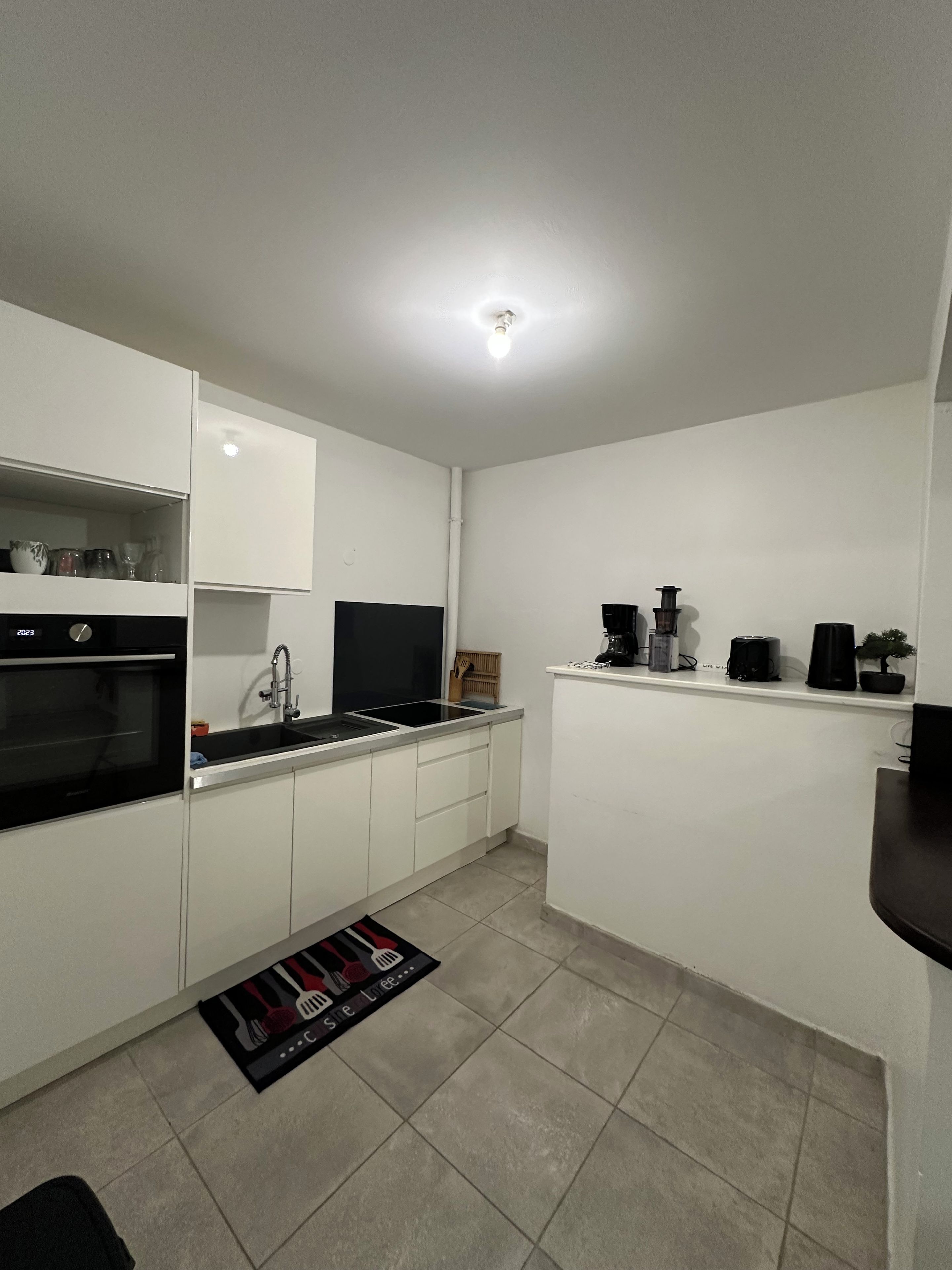 A modern kitchen with white cabinetry, a black oven, a stainless steel sink, and a black countertop.