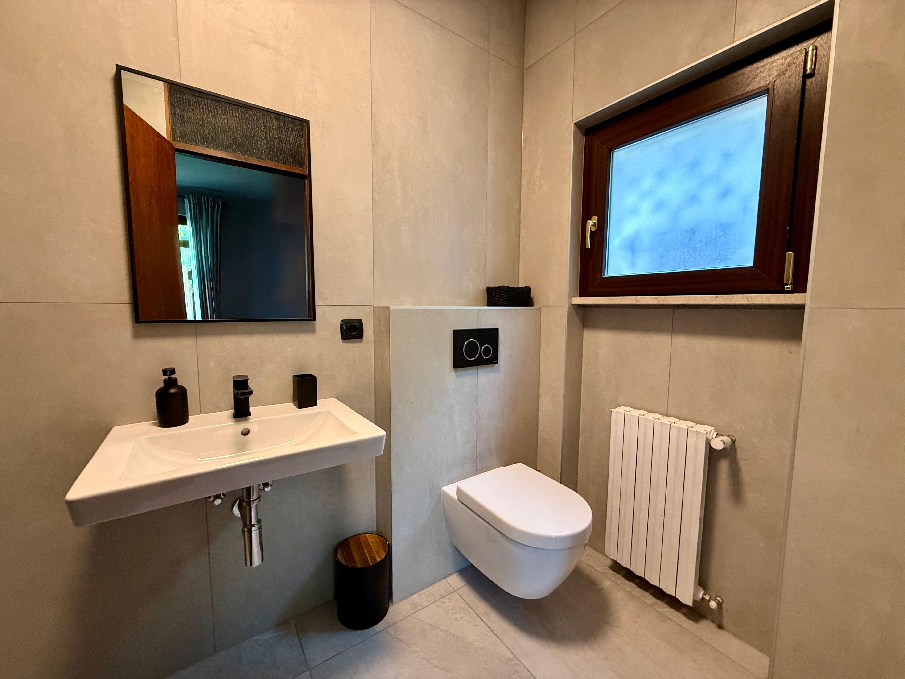 Un bagno moderno con lavandino bianco, vaso, specchio e finestra.