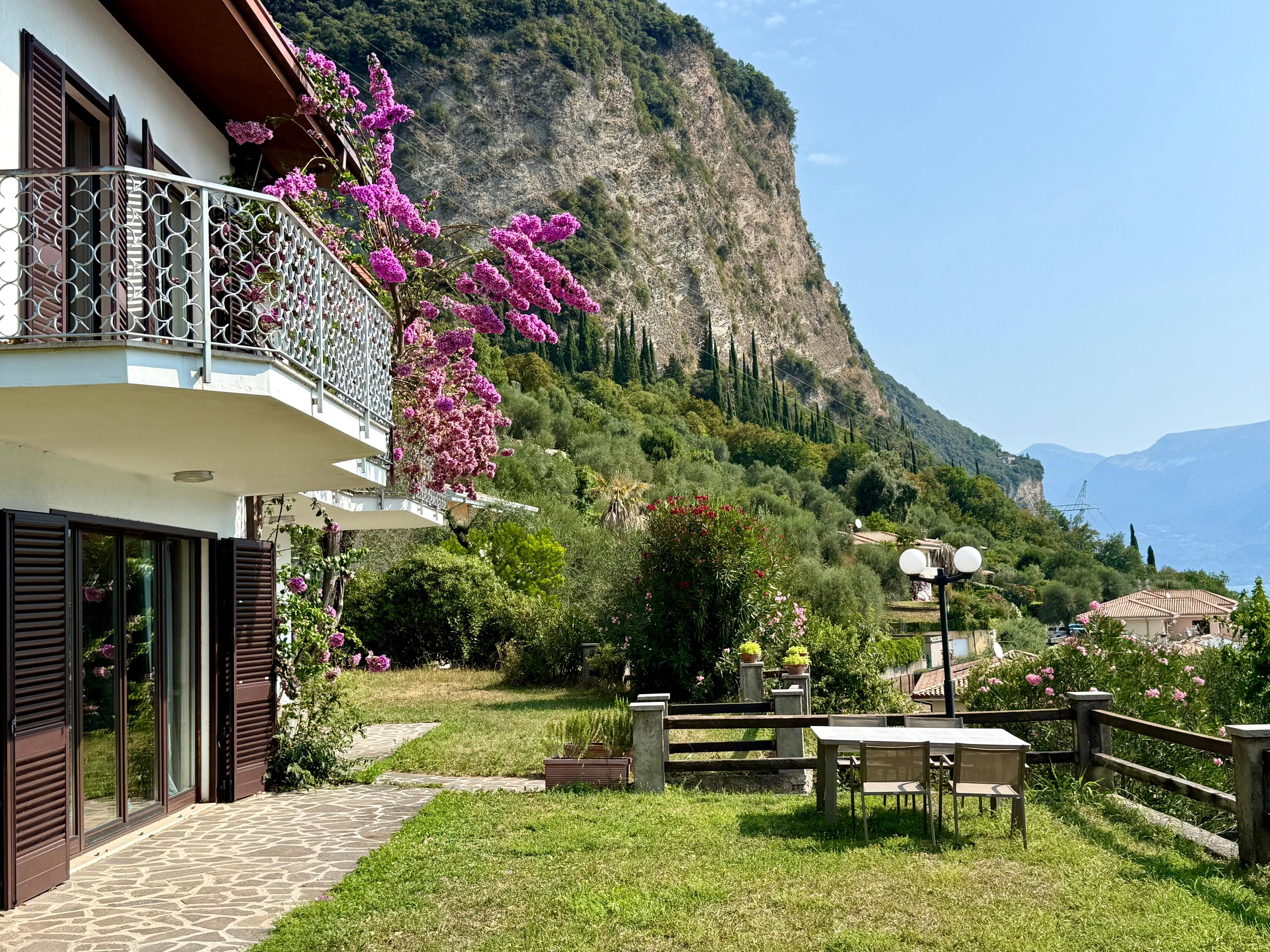 Ein Wohnhaus mit Balkon, einem gepflasterten Weg und Blick auf eine Berglandschaft.