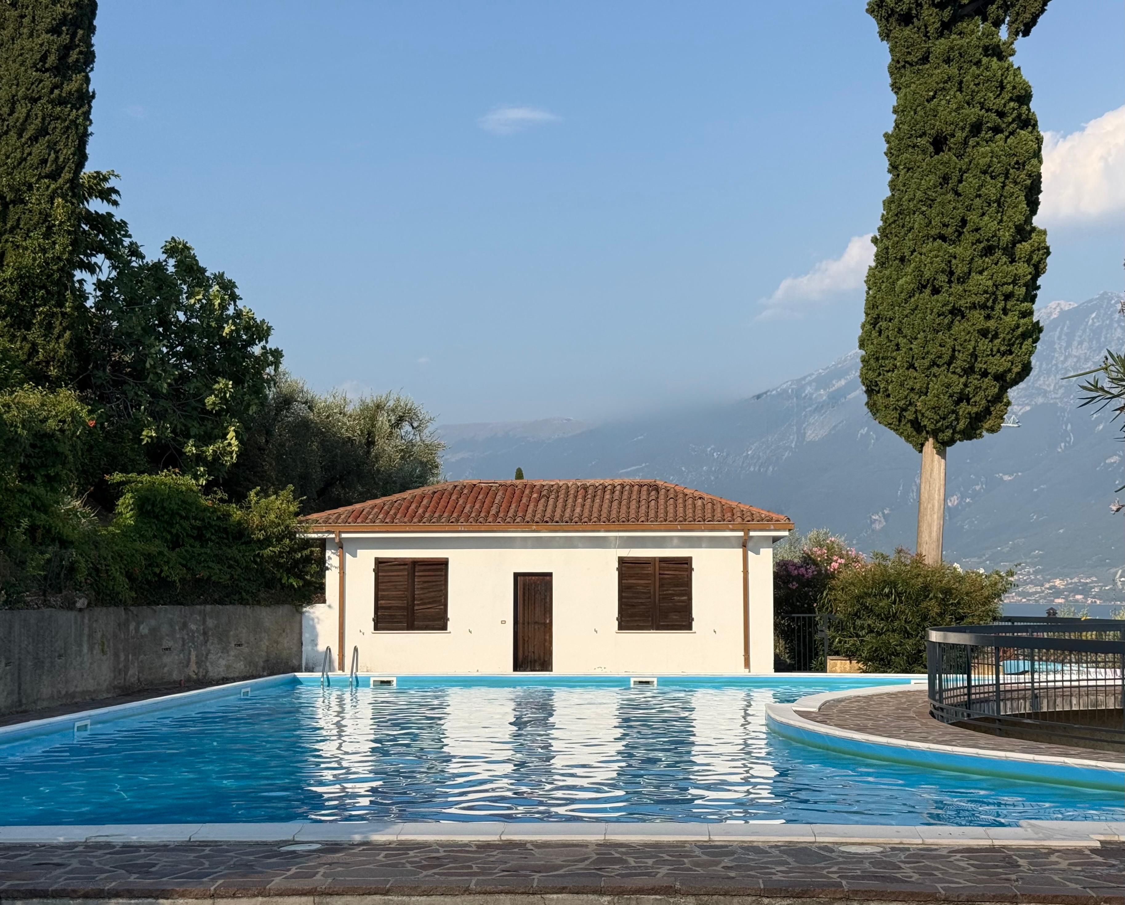 Un piccolo edificio con piscina, immerso tra alberi e montagne.