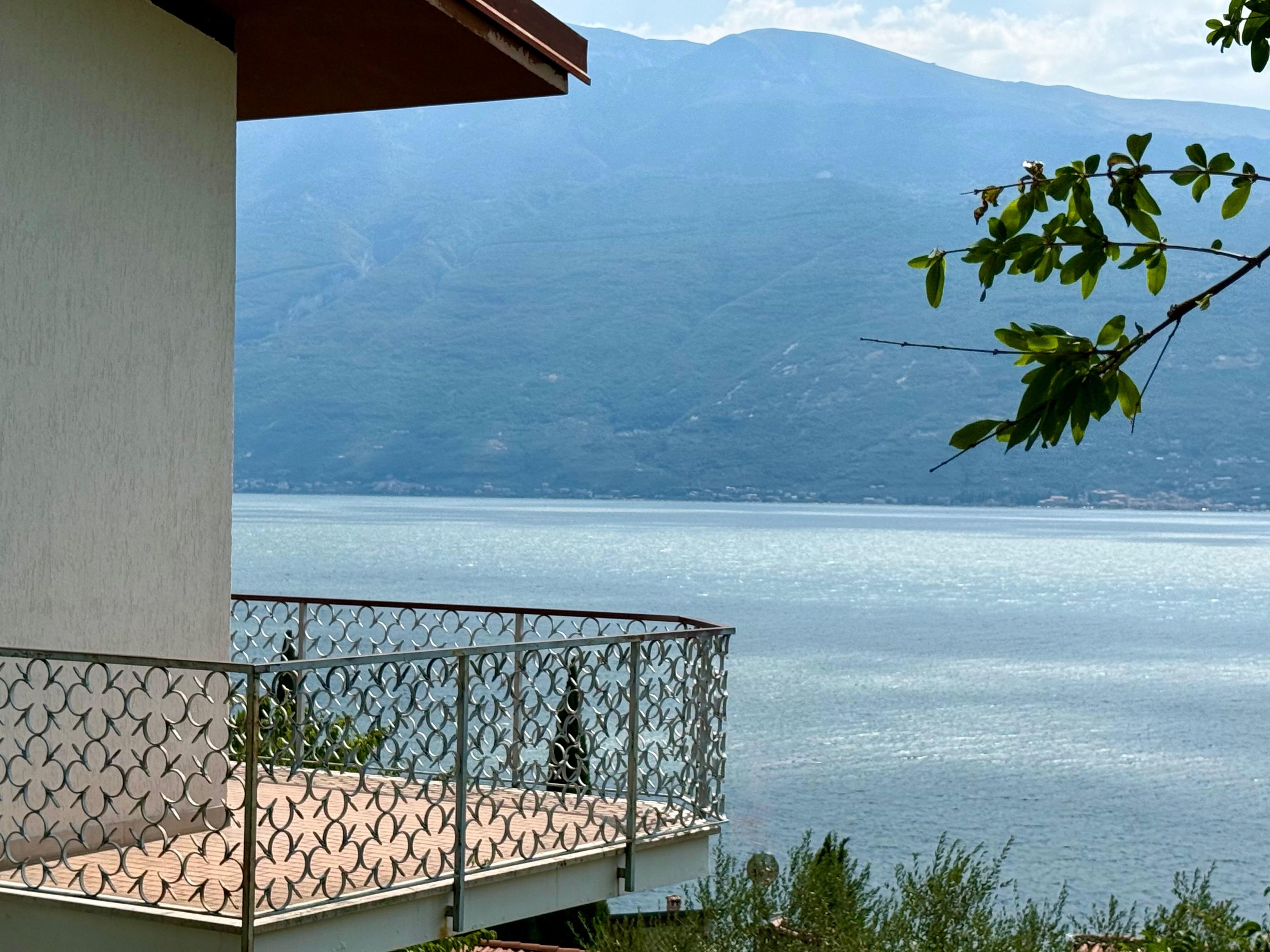 Ein Balkon mit Metallgeländer mit Blick auf einen ruhigen See und ferne Berge.
