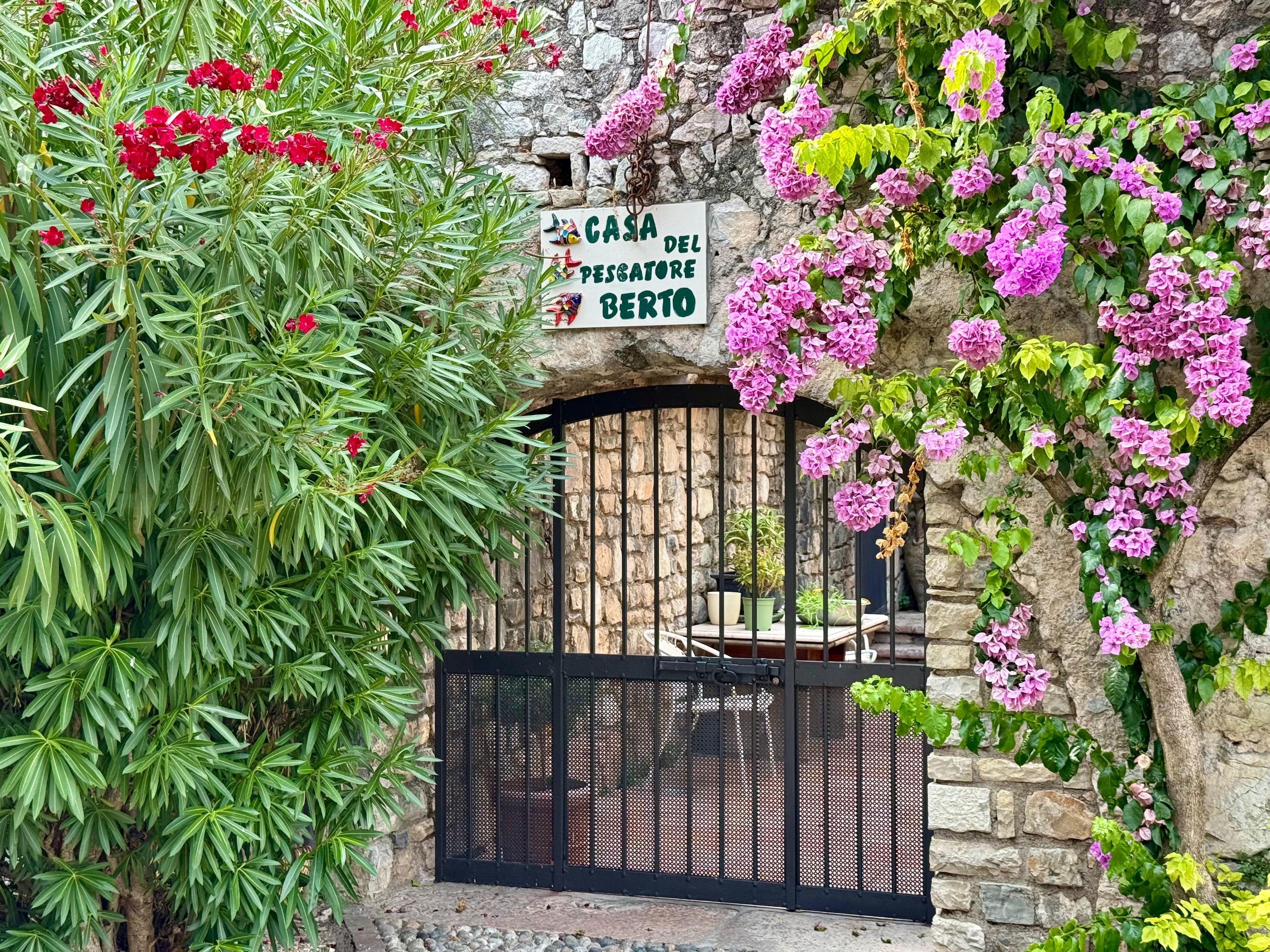 Un mur de pierre avec un portail en métal, une enseigne indiquant « CASA DEL PESCATORI BERTO » et une végétation luxuriante.