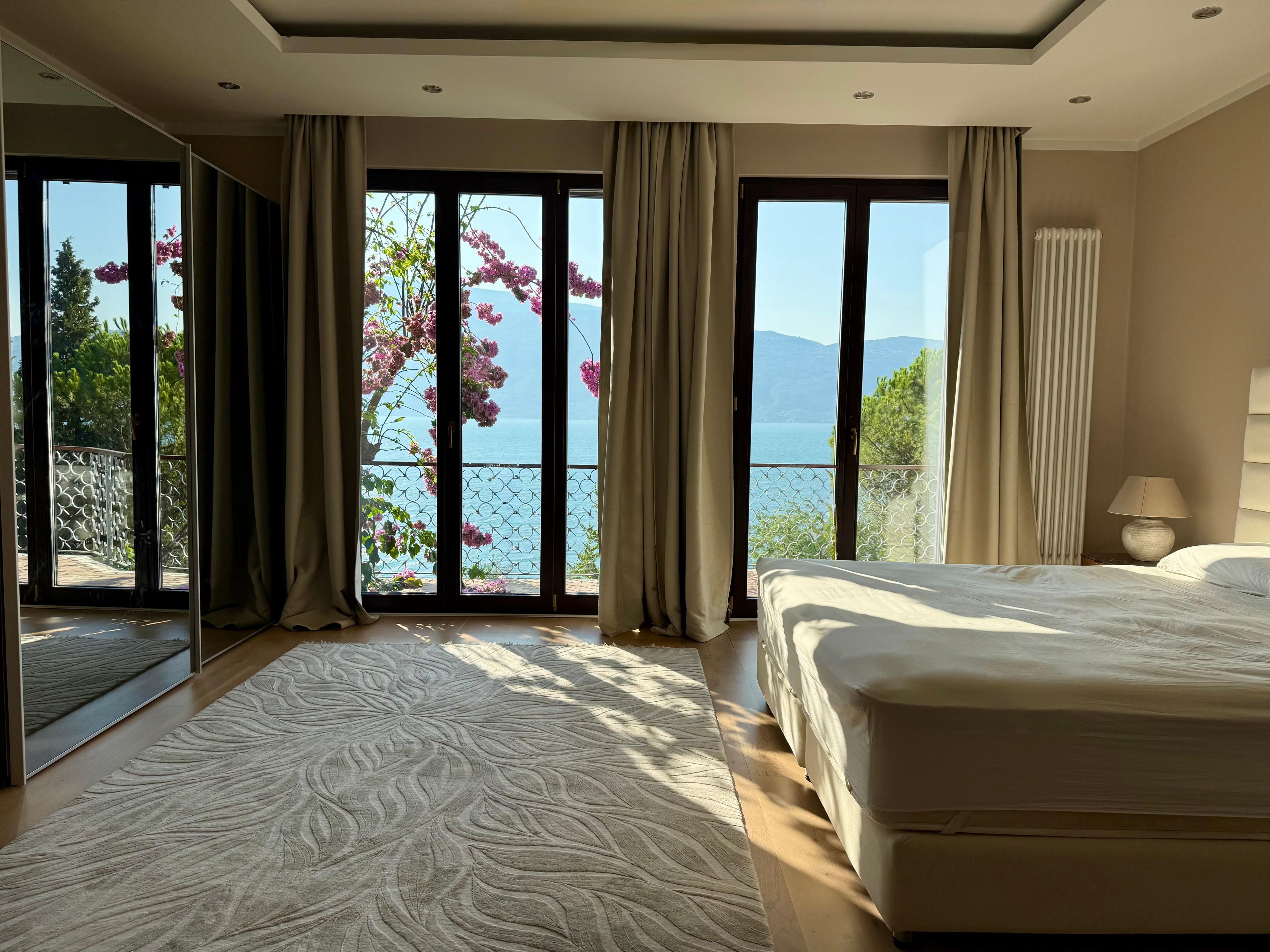 Une chambre avec un grand lit, une vue sur la mer et un balcon agrémenté de fleurs.