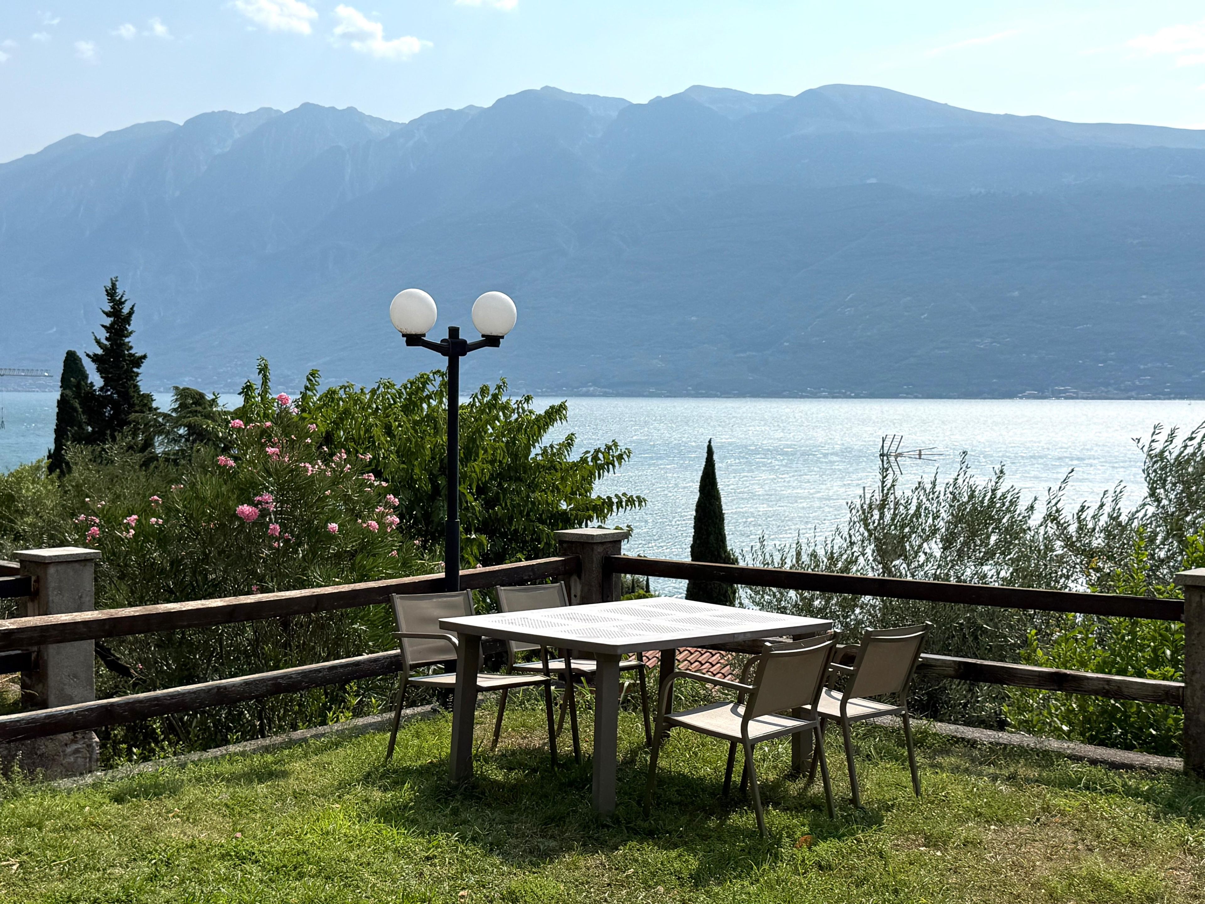 Ein Sitzbereich im Freien mit Tisch und Stühlen, mit Blick auf einen See vor einer Bergkulisse.