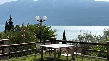Ein Sitzbereich im Freien mit Tisch und Stühlen, mit Blick auf einen See vor einer Bergkulisse.