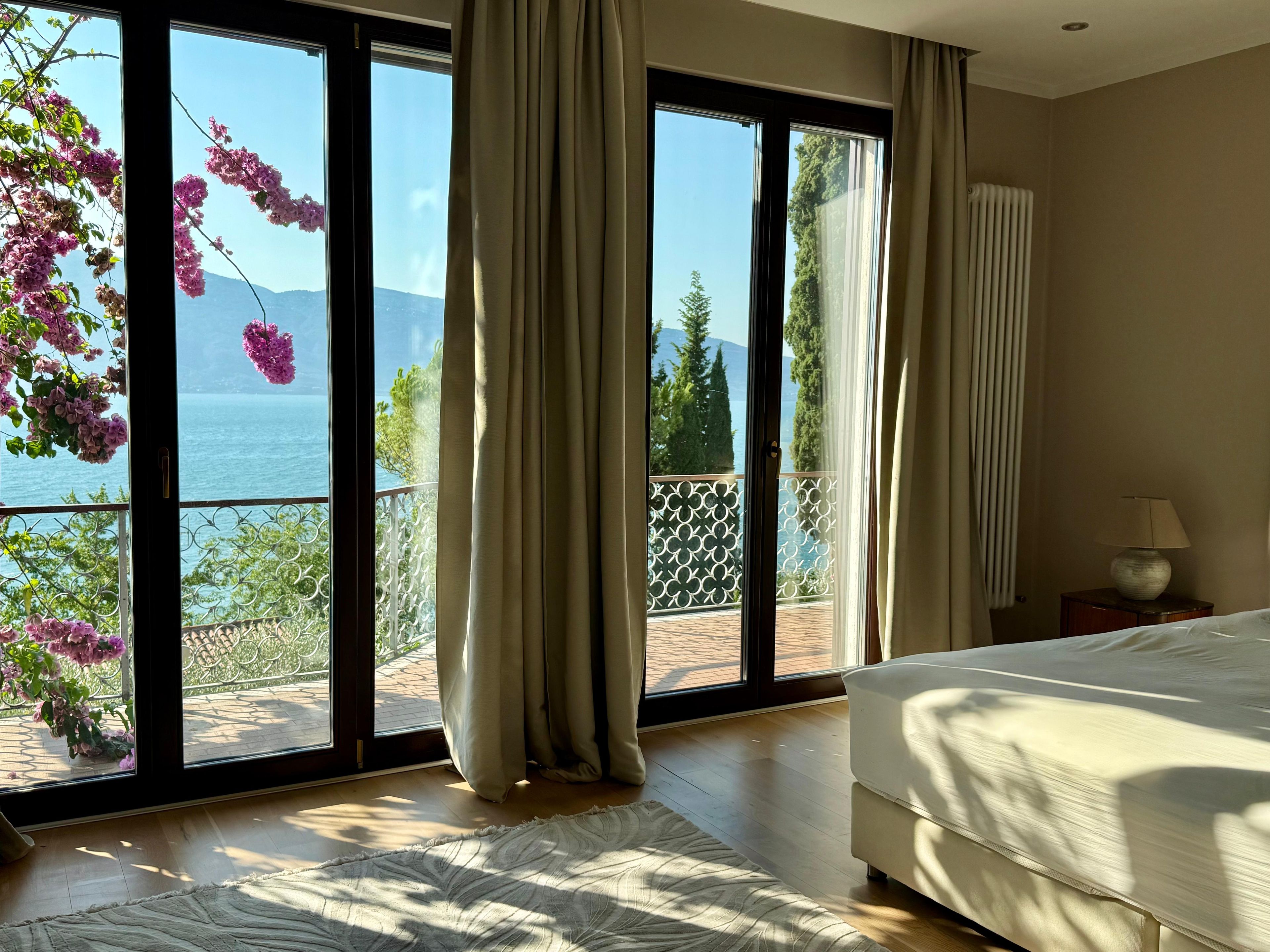 Una camera da letto con un'ampia porta-finestra che si apre su un balcone con vista sul mare e sugli alberi.