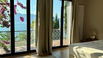 Una camera da letto con un'ampia porta-finestra che si apre su un balcone con vista sul mare e sugli alberi.
