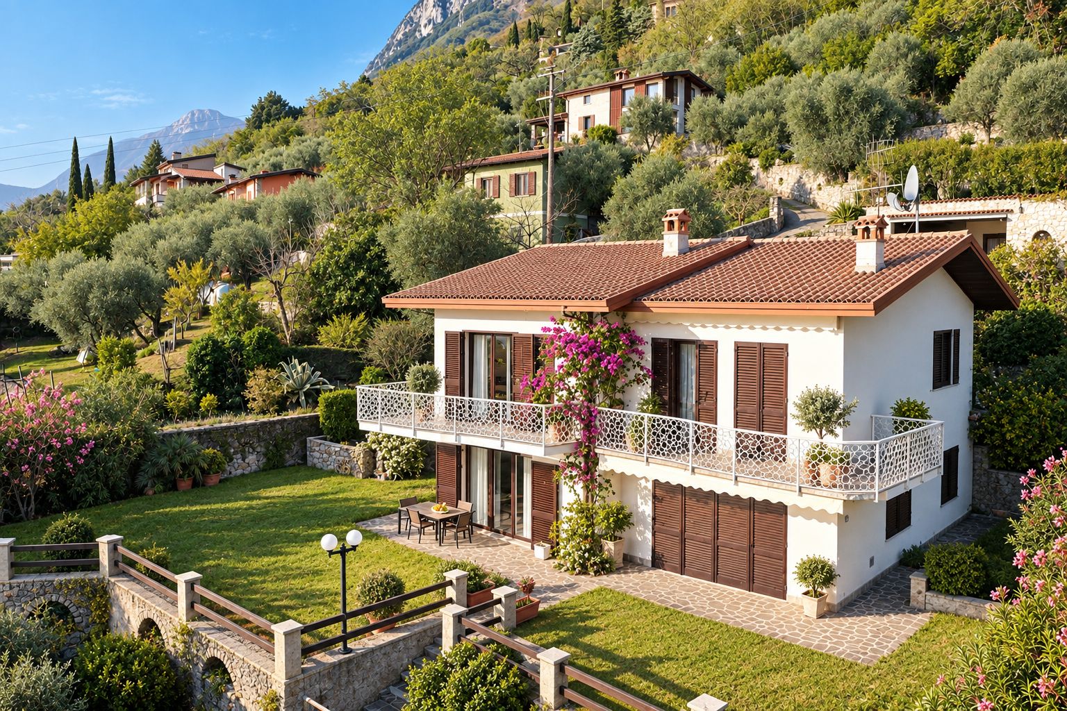 A two-story house with a balcony, surrounded by lush greenery and a mountainous backdrop.
