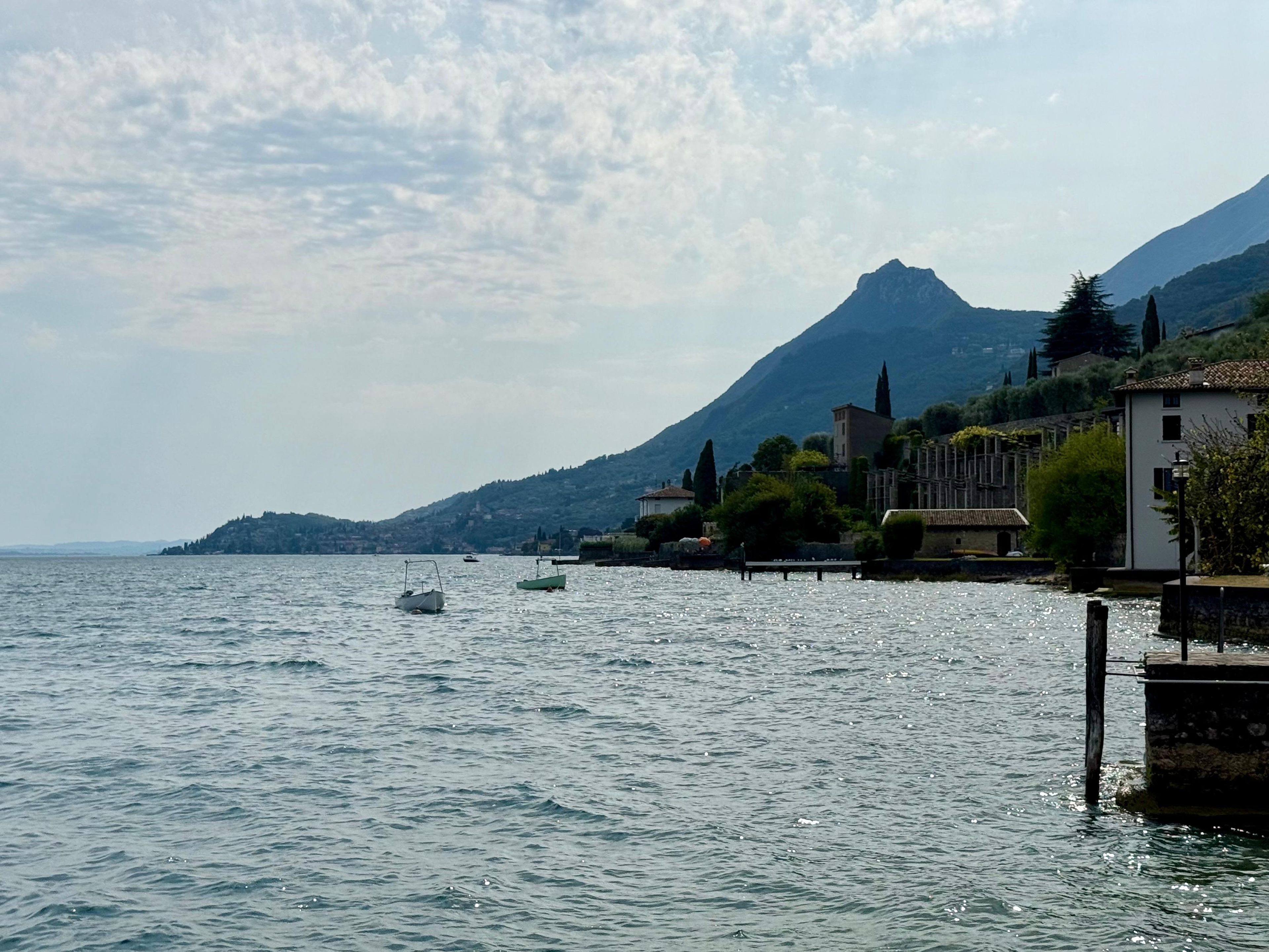 A calm lake with boats, a mountain in the background, and buildings along the shore.