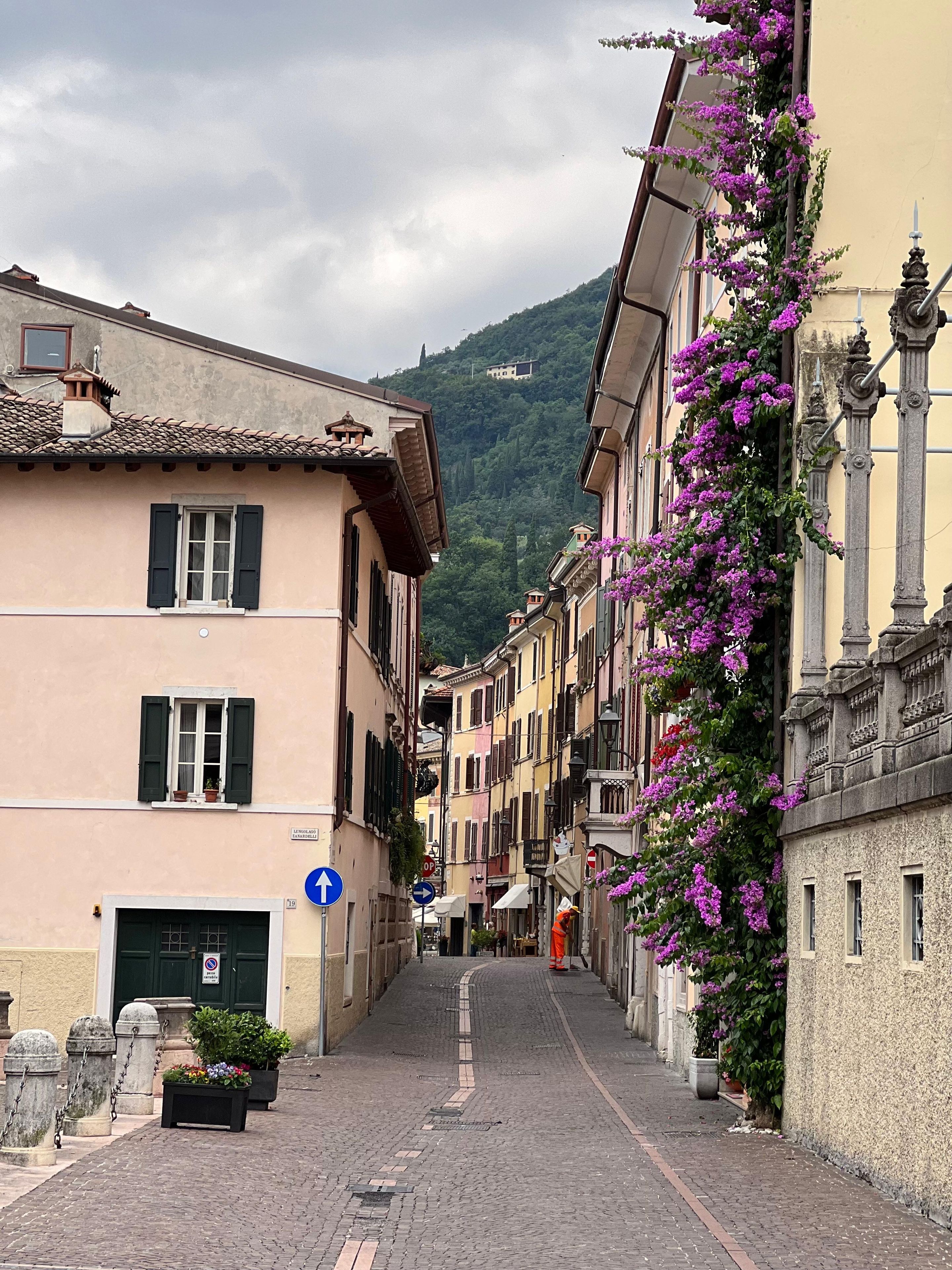 Eine enge Kopfsteinpflasterstraße gesäumt von historischen Gebäuden, ein klarer, blauer Himmel und ein Berg im Hintergrund.