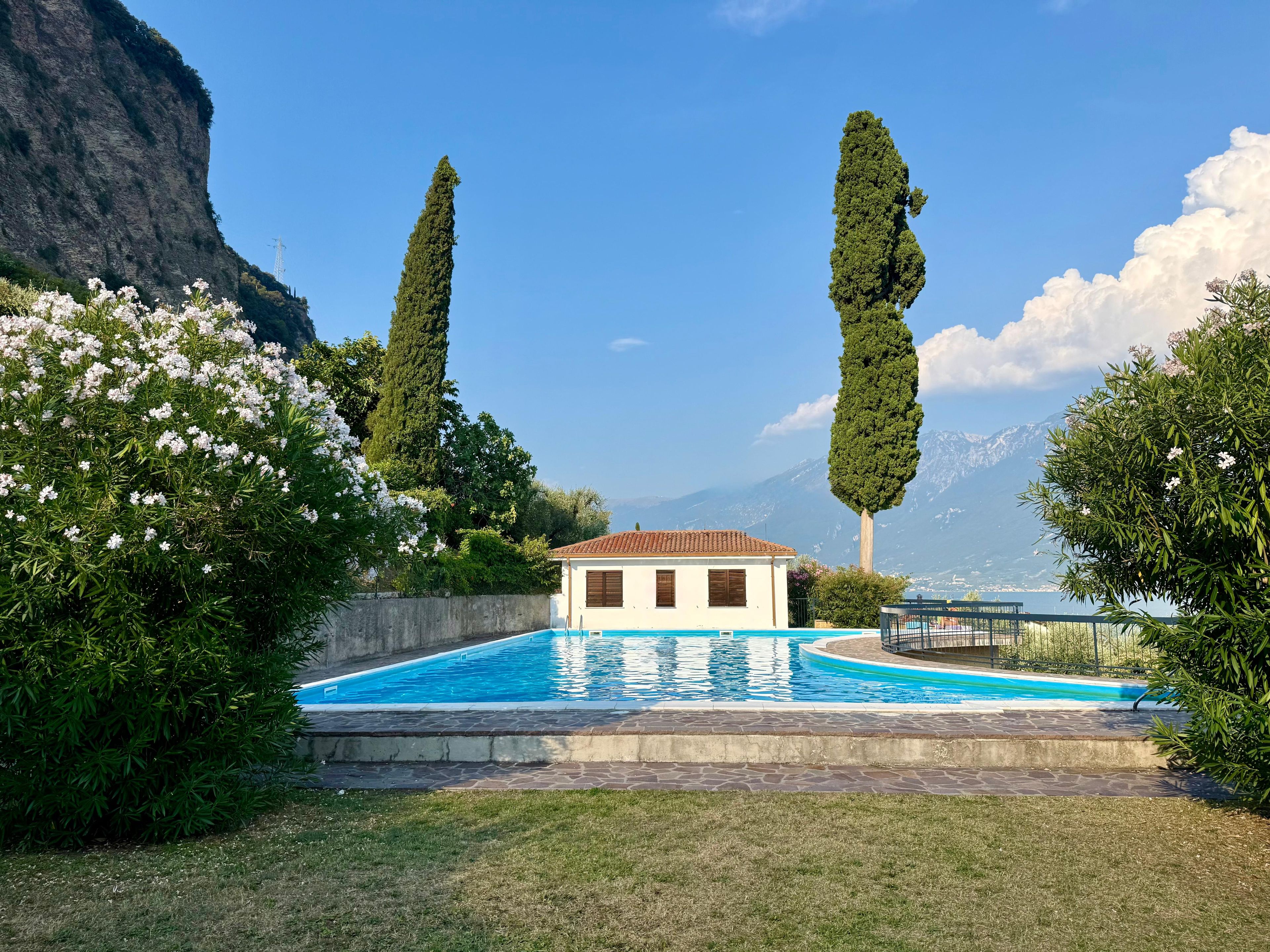 A swimming pool with a small building, surrounded by greenery and mountains in the background.