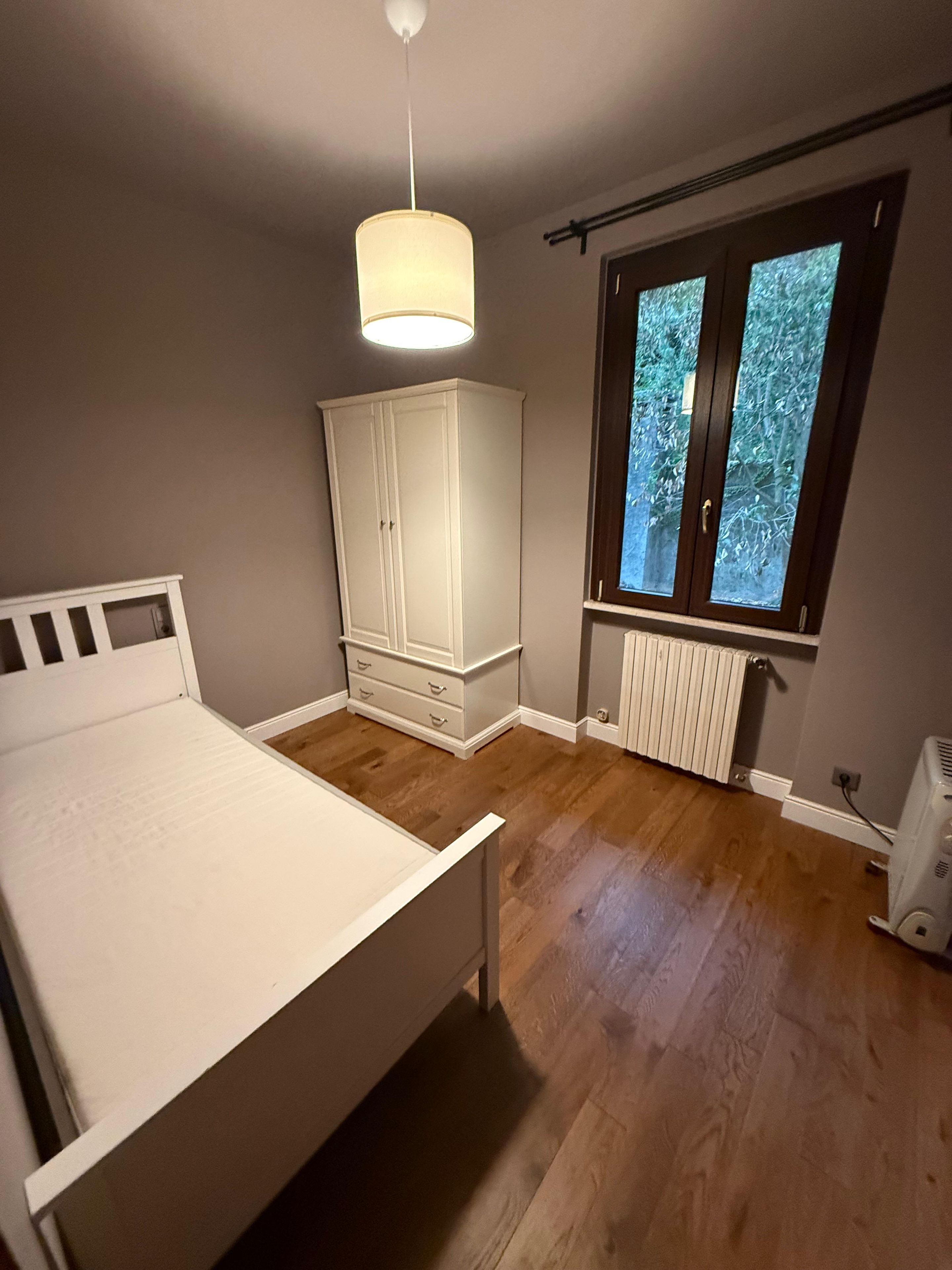 A bedroom with a bed, wardrobe, radiator, and window.