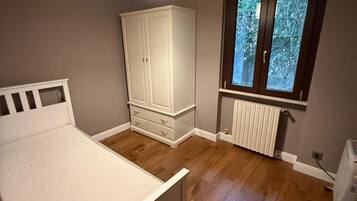 A bedroom with a bed, wardrobe, radiator, and window.