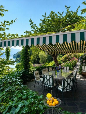 An outdoor dining area with a table and chairs, surrounded by lush greenery and a view of a body of water. - Romantic Villa on Lake Millstatt (Seeboden)