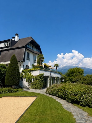Une grande maison avec une pelouse bien entretenue, un chemin en pierre et une vue sur les montagnes en arrière-plan.