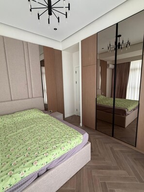 Een moderne slaapkamer met een groot bed, een kledingkast, een spiegel en een plafondlamp.
