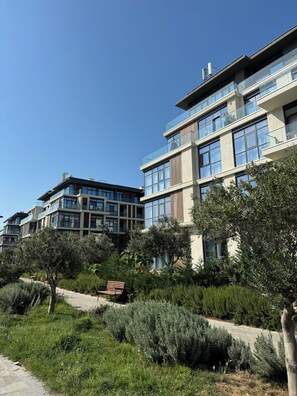 Een modern gebouw met meerdere balkons en grote ramen, omringd door groen en een verhard pad.