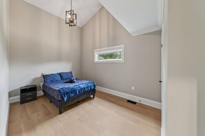 Ein Schlafzimmer mit einem Bett, einem Nachttisch, einer Kommode, einem Fenster und einer Deckenleuchte.