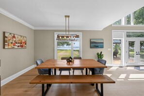 Un comedor con mesa y sillas de madera, una lámpara colgante y vistas al exterior a través de un gran ventanal.