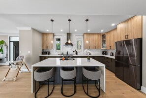 A modern kitchen with a central island, bar stools, stainless steel appliances, and pendant lighting.