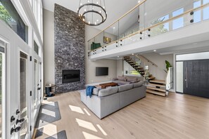 A spacious living area with a stone fireplace, a large gray sofa, and a modern staircase.