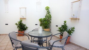 Um pátio com mesa redonda e quatro cadeiras, rodeado por plantas em vasos e painéis de macramé.