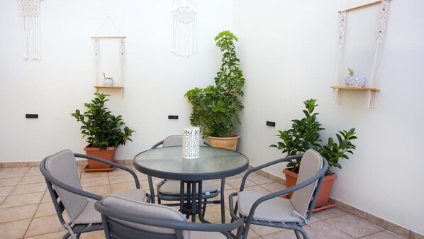 A patio with a round table and four chairs, surrounded by potted plants and macramé wall hangings.