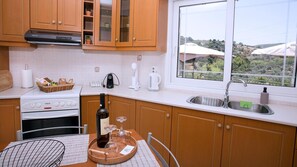 A kitchen with wooden cabinets, a stove, a sink, and a window with a view of greenery.