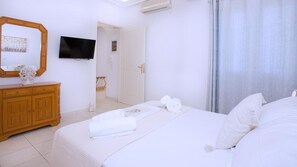 Habitación de hotel con una cama, un aparador de madera, un televisor y un baño visible a través de una puerta abierta.