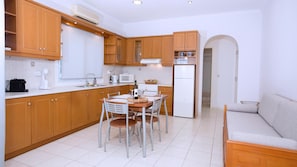 Una cocina funcional con armarios de madera, una mesa de comedor con sillas, un refrigerador y un sofá en una esquina.