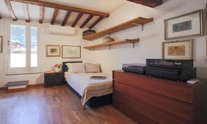 Quarto com cama, cómoda de madeira, estantes com livros e quadros na parede.
