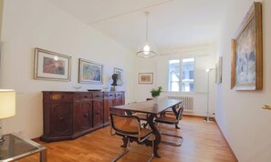 Uma sala de jantar com mesa e cadeiras de madeira, um armário e obras de arte emolduradas nas paredes.