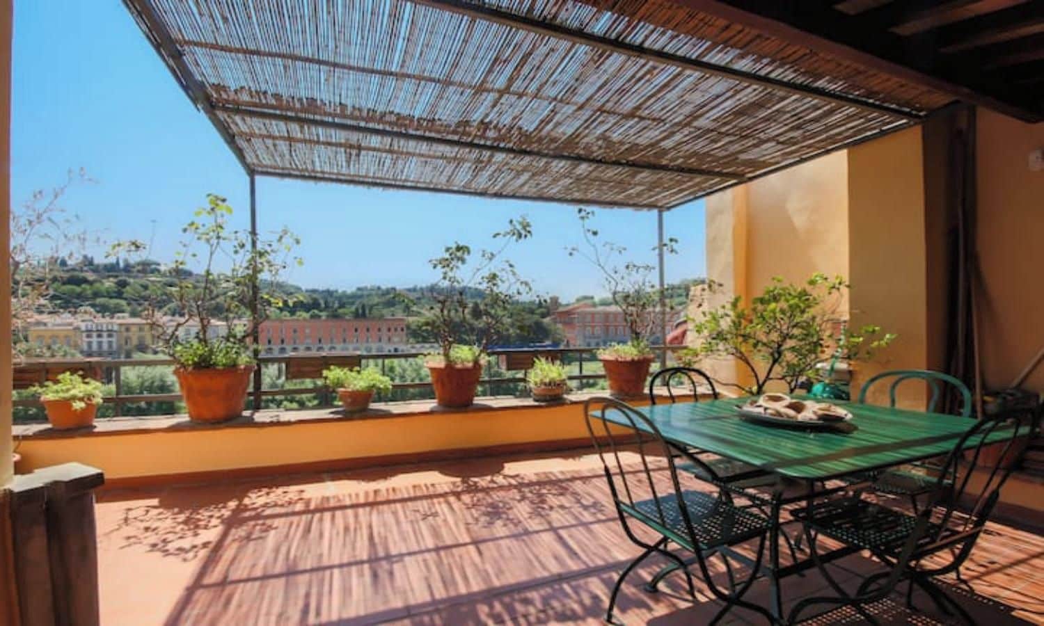 A balcony with a table and chairs, potted plants, and a view of buildings in the distance.