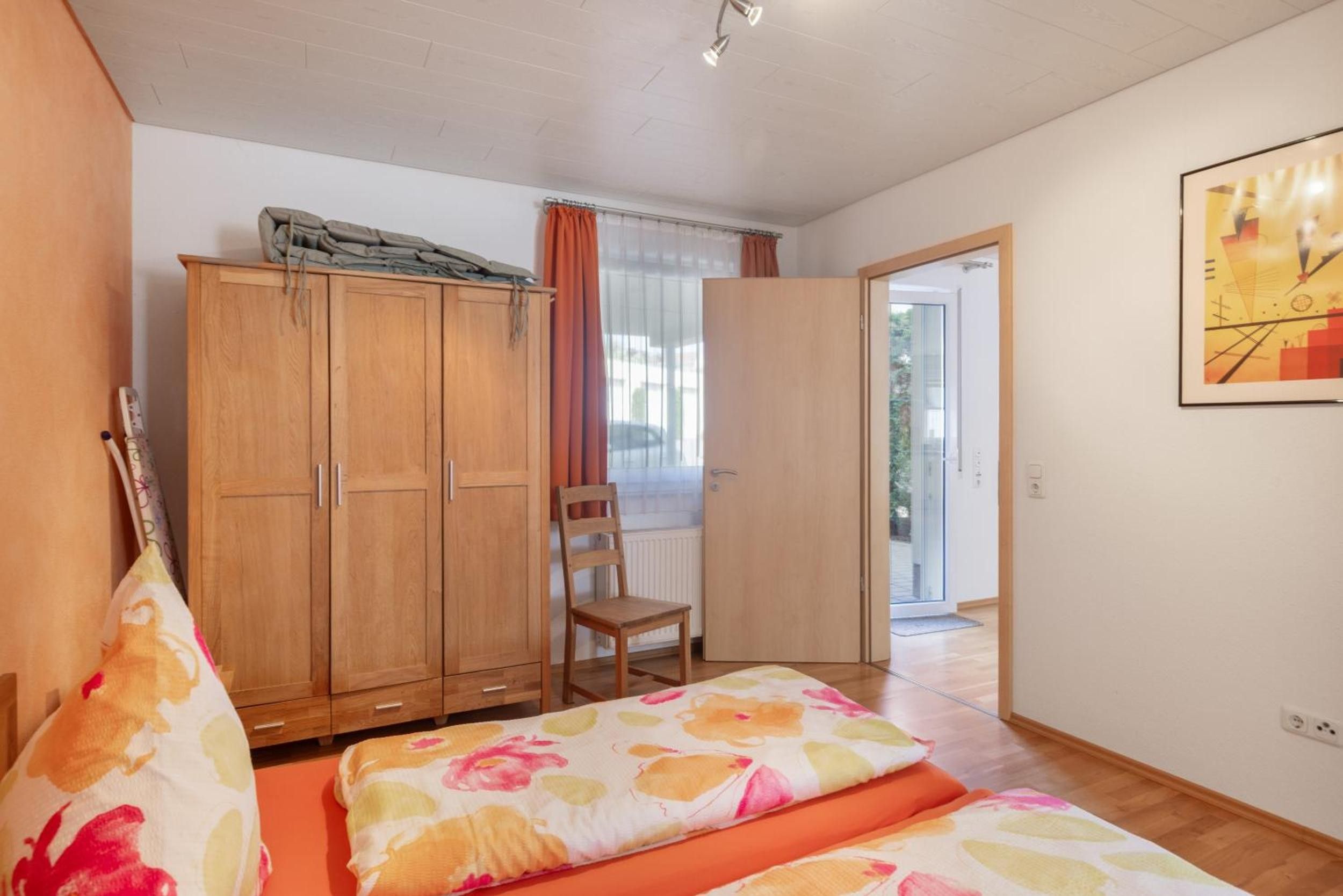 Ein Zimmer mit einem Bett, einem Sessel, einem Kleiderschrank und einer Tür zu einem Außenbereich.