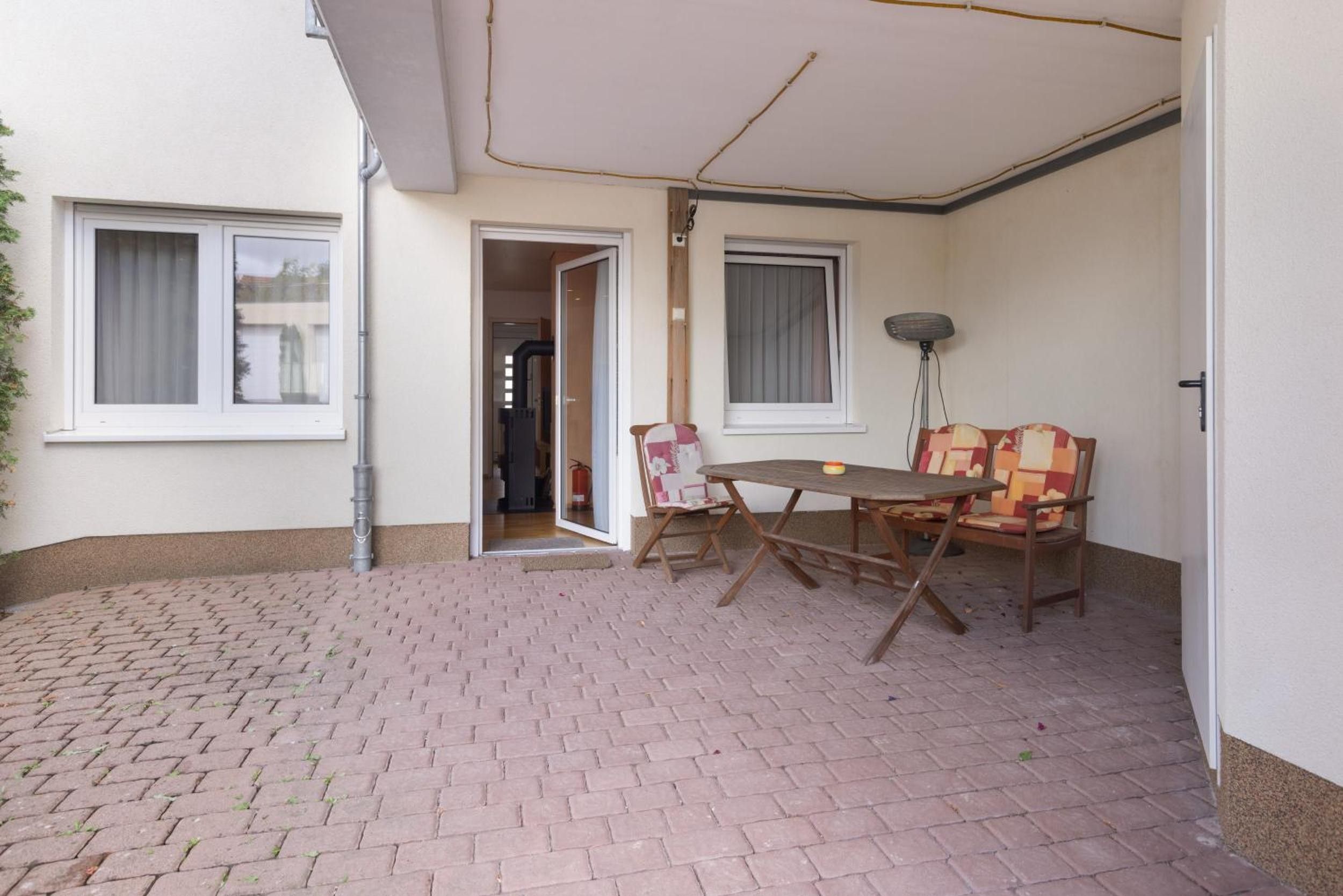 Ein überdachter Patio-Bereich mit Backsteinboden, einem Tisch und Stühlen sowie einer Tür zu einem Innenraum.