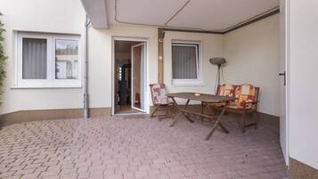 Ein überdachter Patio-Bereich mit Backsteinboden, einem Tisch und Stühlen sowie einer Tür zu einem Innenraum.