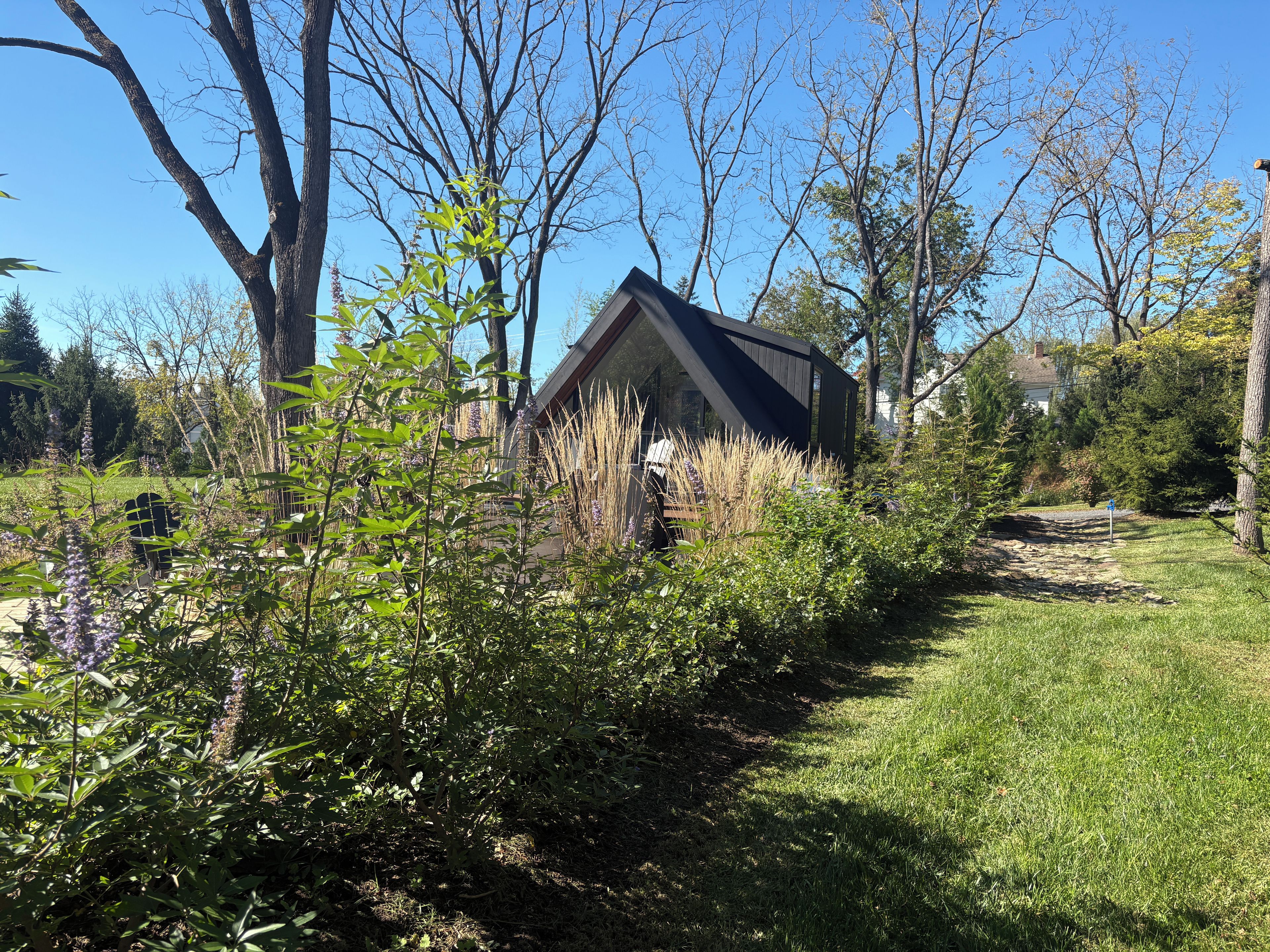 Une maison avec un toit en pente, entourée d’un jardin où poussent différentes plantes et arbres.