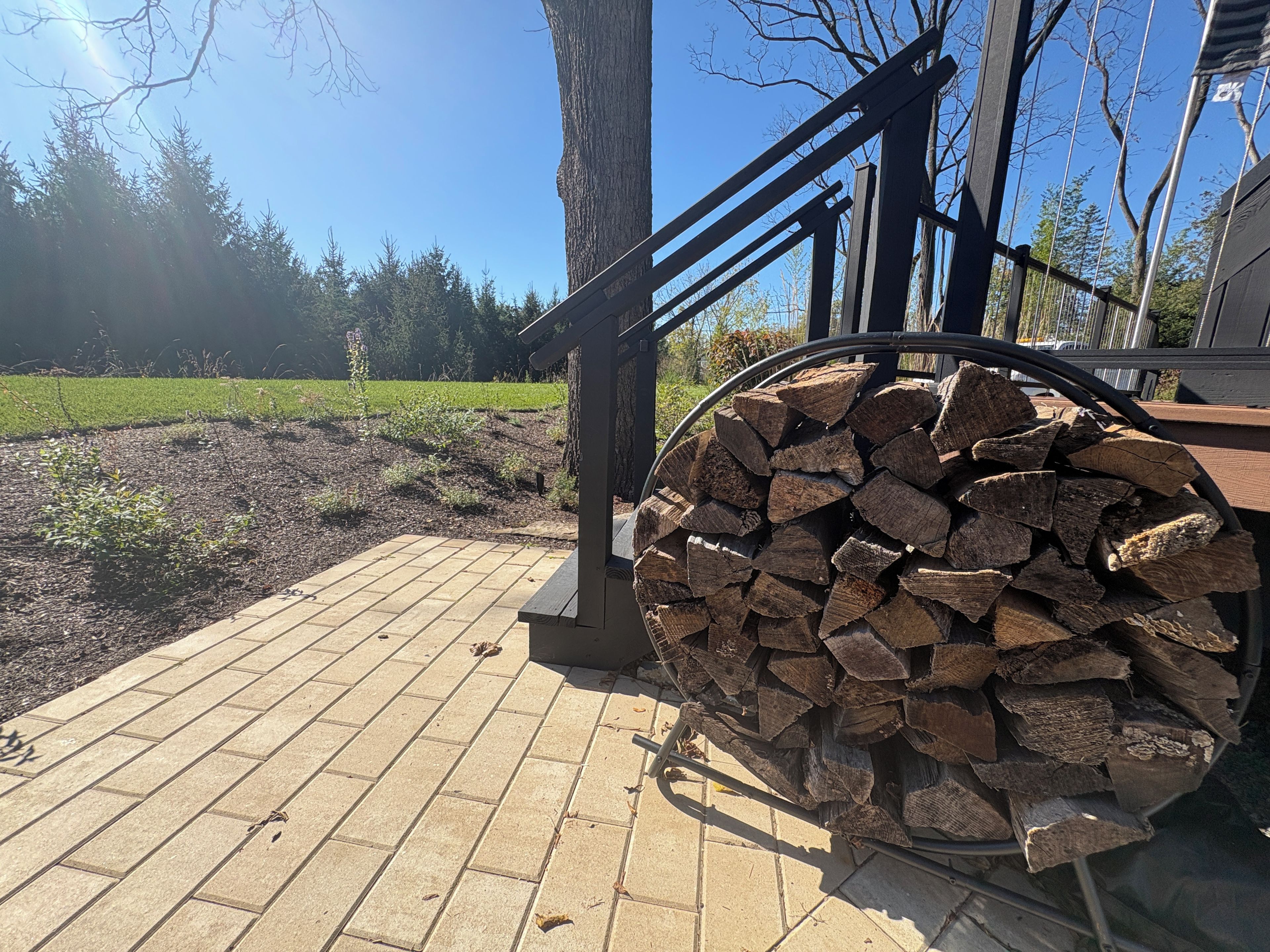Une terrasse en bois avec une rambarde en métal et une pile de bois de chauffage.