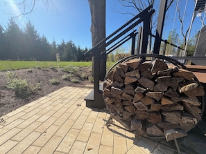 Una terraza de madera con barandilla metálica y una pila de leña.