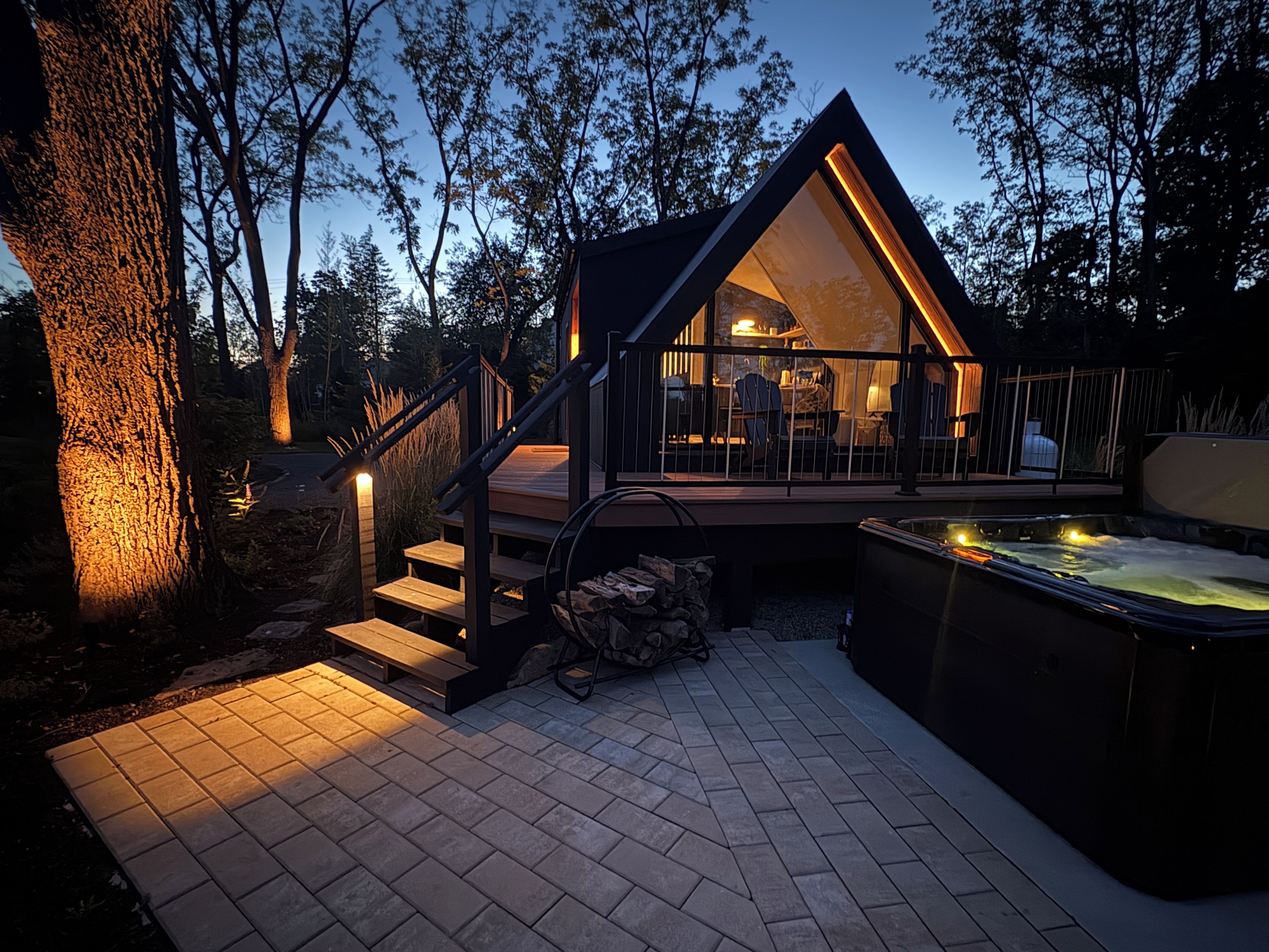 Une cabane moderne avec une façade en verre, une terrasse en bois et un jacuzzi.