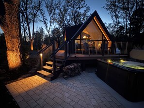 A modern cabin with a glass facade, wooden deck, and a hot tub.