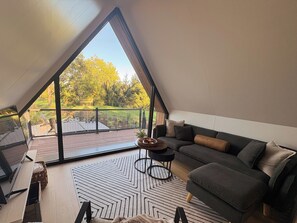 Un dormitorio estilo loft moderno con un tragaluz grande, un sofá, una mesita redonda y vistas a una terraza y árboles.