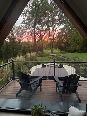 A deck with outdoor furniture, a view of trees, and a sunset.