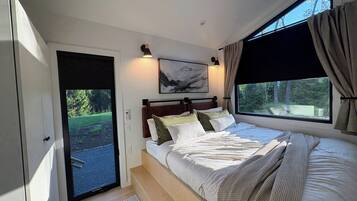 Ein Schlafzimmer mit einem Bett, einem Gemälde, einem Fenster mit Vorhängen und Blick ins Grüne.