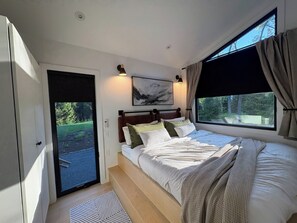 A bedroom with a bed, a painting, a window with curtains, and a view of greenery outside.