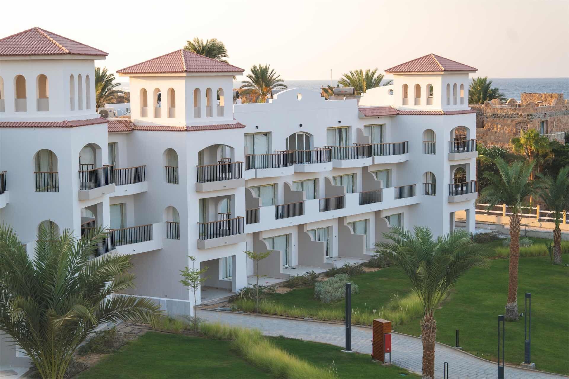 A multi-story hotel with balconies, a paved walkway, and palm trees.