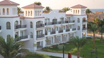 A multi-story hotel with balconies, a paved walkway, and palm trees.