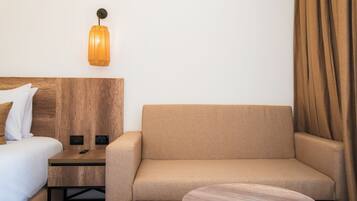 A hotel room with a bed, a sofa, a small table, and a wall-mounted lamp.